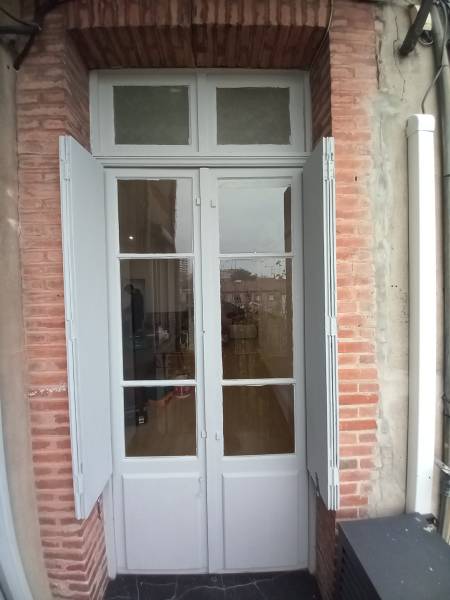 Une porte-fenêtre en bois simple vitrage d'époque, esthétiquement charmante mais source de déperditions énergétiques et de nuisances sonores en centre-ville de Toulouse.