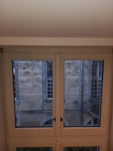 L'ancien imposte fixe en bois avant la rénovation. Cette configuration empêchait toute aération, nécessitant le changement de menuiserie pour améliorer le confort de la chambre.